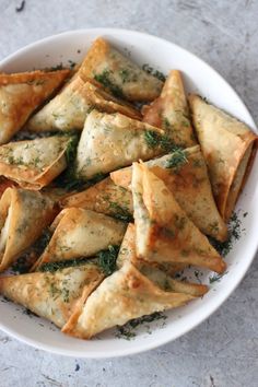 a white bowl filled with dumplings covered in cheese and herbs on top of a table