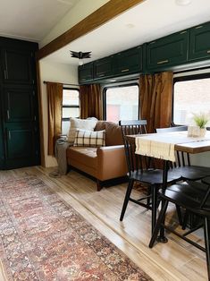 a living room and dining area in an rv with wood floors, green walls, and black cabinets