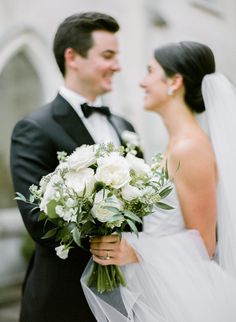 a bride and groom smile at each other as they stand in front of a building