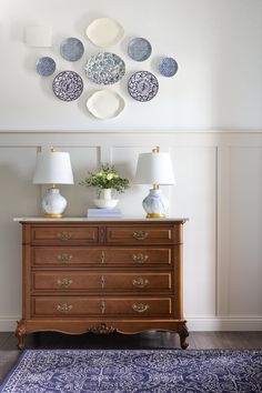 a dresser with several plates mounted on the wall above it and a rug in front of it