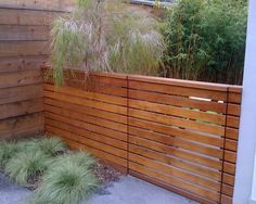 a wooden fence in front of a house with grass growing on the ground and bushes behind it