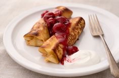 crepes with cherry sauce and yogurt on a white plate next to a fork