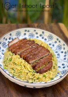 a white and blue plate topped with meat and rice on top of a wooden table