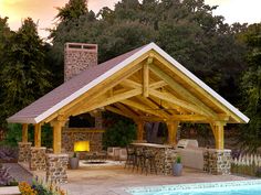 an outdoor kitchen and bar area next to a swimming pool with fire pit in the middle