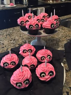 cupcakes with pink frosting and eyes are on a cake plate in the kitchen