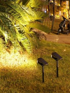 two solar powered lights in the grass next to a motor scooter and palm tree