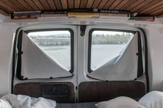 the inside of a camper with two windows and pillows on it's bed