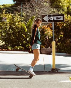 a woman riding a skateboard down a street next to a one way road sign