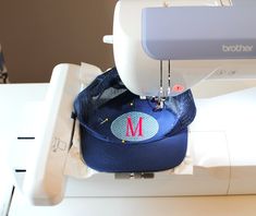 a sewing machine with a blue hat on it's head and the letter m