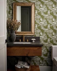 a bathroom with a sink, mirror and wallpaper in green color scheme on the walls