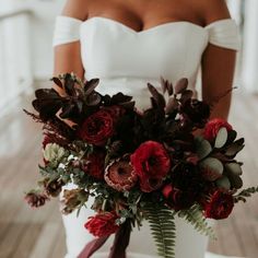 a woman in a white dress holding a bouquet of red and green flowers on her wedding day