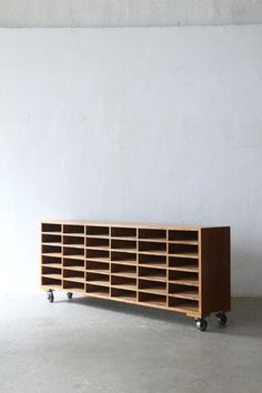 a wooden shelf sitting on top of a cement floor next to a white wall and black wheels