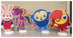 three paper cutouts of cartoon characters on a shelf with one holding a rainbow and the other pointing at it