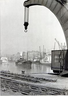 an old photo of a crane lifting cargo onto the water from a bridge over train tracks