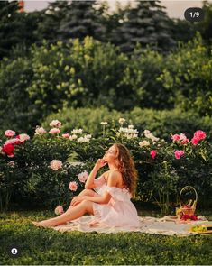 a young woman sitting on top of a blanket in the grass next to pink flowers