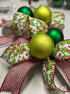 two green and red ornaments on top of each other next to ribboned bows with bells