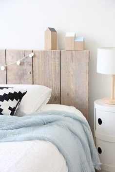 a bed with white sheets and pillows in a room next to a night stand that has books on it