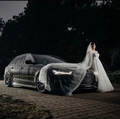 a woman in a wedding dress standing next to a car with a veil on it