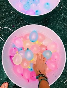 two bowls with balloons floating in them and someone's hand reaching for the bowl