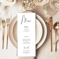 a table setting with place cards, silverware and white flowers on the table top