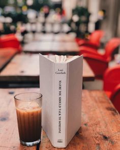 a book sitting on top of a wooden table next to a glass filled with liquid