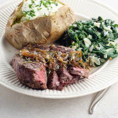 a white plate topped with steak, potatoes and spinach next to a baked potato