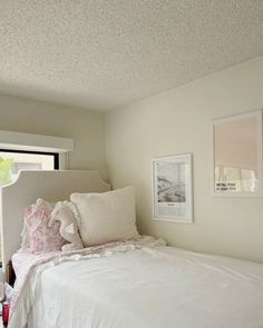 a white bed sitting in a bedroom next to a window with pictures on the wall