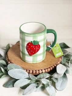 a green and white mug with a strawberry on it sitting on top of a wooden tray