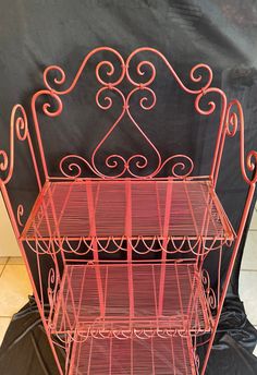 three tiered metal rack with red paint on the top and bottom shelf, in front of a black backdrop