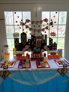 the table is set up for a birthday party in front of a window with cityscape on it