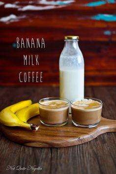 two glasses of banana milk next to a bottle of coffee on a wooden tray with bananas