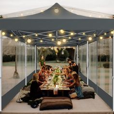 a group of people sitting at a table under a tent with lights on the ceiling