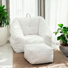 a white chair and footstool in front of a window with potted plants