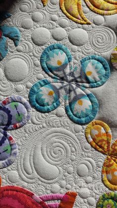 an embroidered quilt with colorful flowers and leaves on the side, along with circles in the center