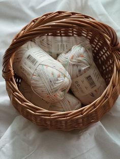 several balls of yarn in a wicker basket on a white cloth covered bed sheet