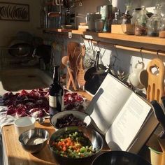 an open book sitting on top of a wooden table next to bowls and pans