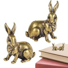 two gold rabbits sitting next to each other on top of a red book and an open book