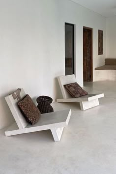 two white benches sitting next to each other on top of a cement floor in an empty room