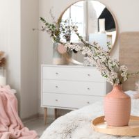 a pink vase sitting on top of a bed next to a white dresser and mirror