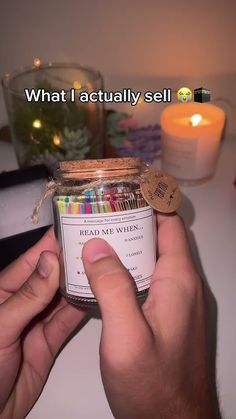 a person holding a jar filled with lots of colored pencils next to a lit candle