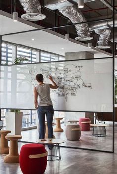 a man writing on a whiteboard in an office with lots of tables and stools