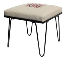 a small foot stool with an embroidered design on the top and legs, sitting against a white background