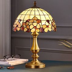 a lamp that is on top of a table next to a book and pen with eyeglasses