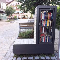 a book case sitting on the side of a road next to a park bench