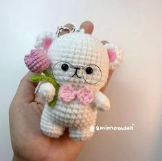 a small crocheted teddy bear with glasses and a flower in it's hand