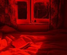 a red light shining on a bed in a dark room with curtains and window sill