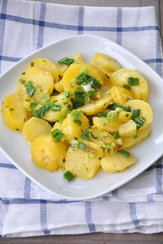 a white plate topped with potatoes covered in green onions and seasoning next to a blue checkered napkin