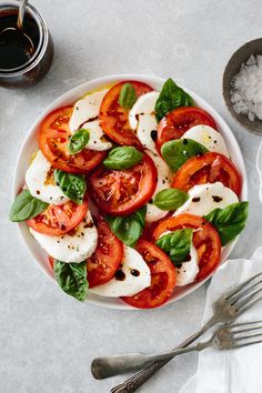 a white plate filled with sliced tomatoes and basil on top of rice next to spoons