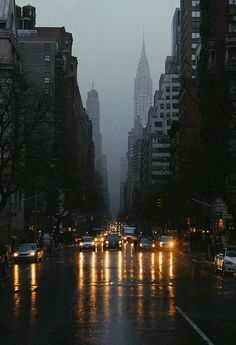 a city street at night with cars driving on the road and tall buildings in the background