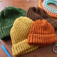 three knitted hats sitting on top of a wooden table next to scissors and yarn